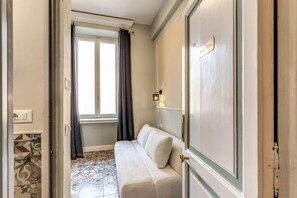 Une pièce avec un canapé beige, une fenêtre avec des rideaux, un sol carrelé et une porte portant l’inscription « Suite Krug ».
