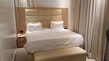A hotel room with a bed, a bedside table, a lamp, and a window with curtains.
