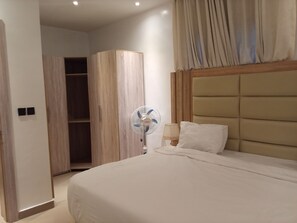 Un dormitorio con cama, lámpara de noche, ventilador de pared y armario.