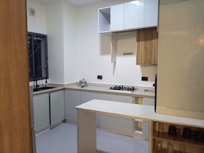 A kitchen with white cabinets, a gas stove, a sink, and a wooden shelf. - Vision Luxury Apartment (Lekki)