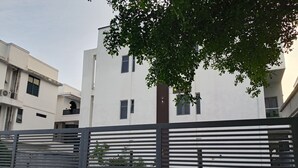 En moderne bygning med hvid facade, flere vinduer og et træ i forgrunden.