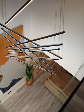 A modern staircase with a geometric metal railing design, a potted plant, and a wooden floor. - Vision Luxury Apartment (Lekki)