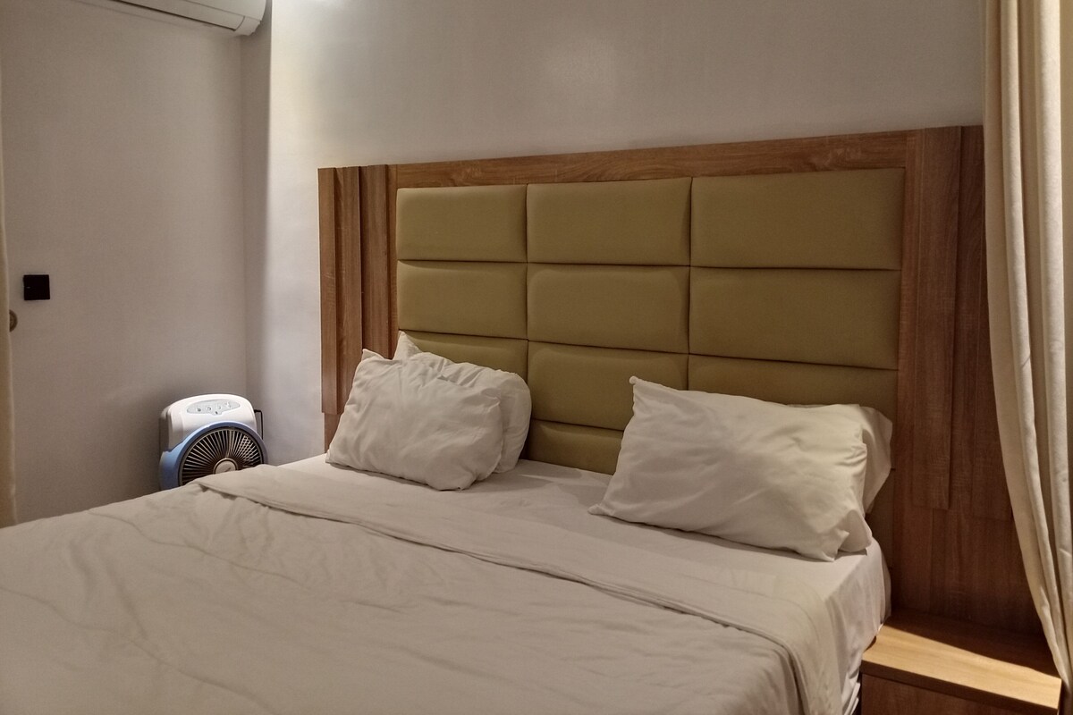 Habitación de hotel con cama, mesita de noche, aire acondicionado y ventana con cortinas.