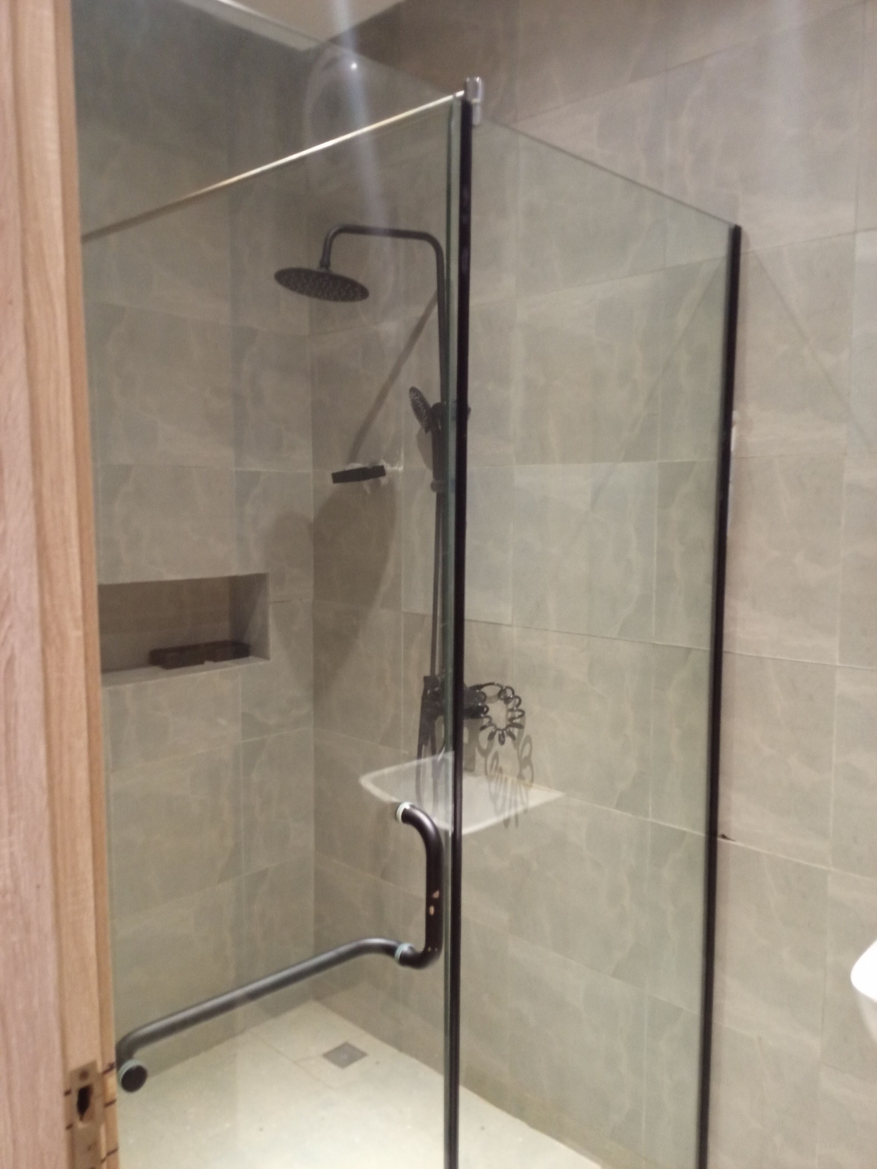 A glass-enclosed shower area with a handheld showerhead, a wall-mounted faucet, and a shelf.
