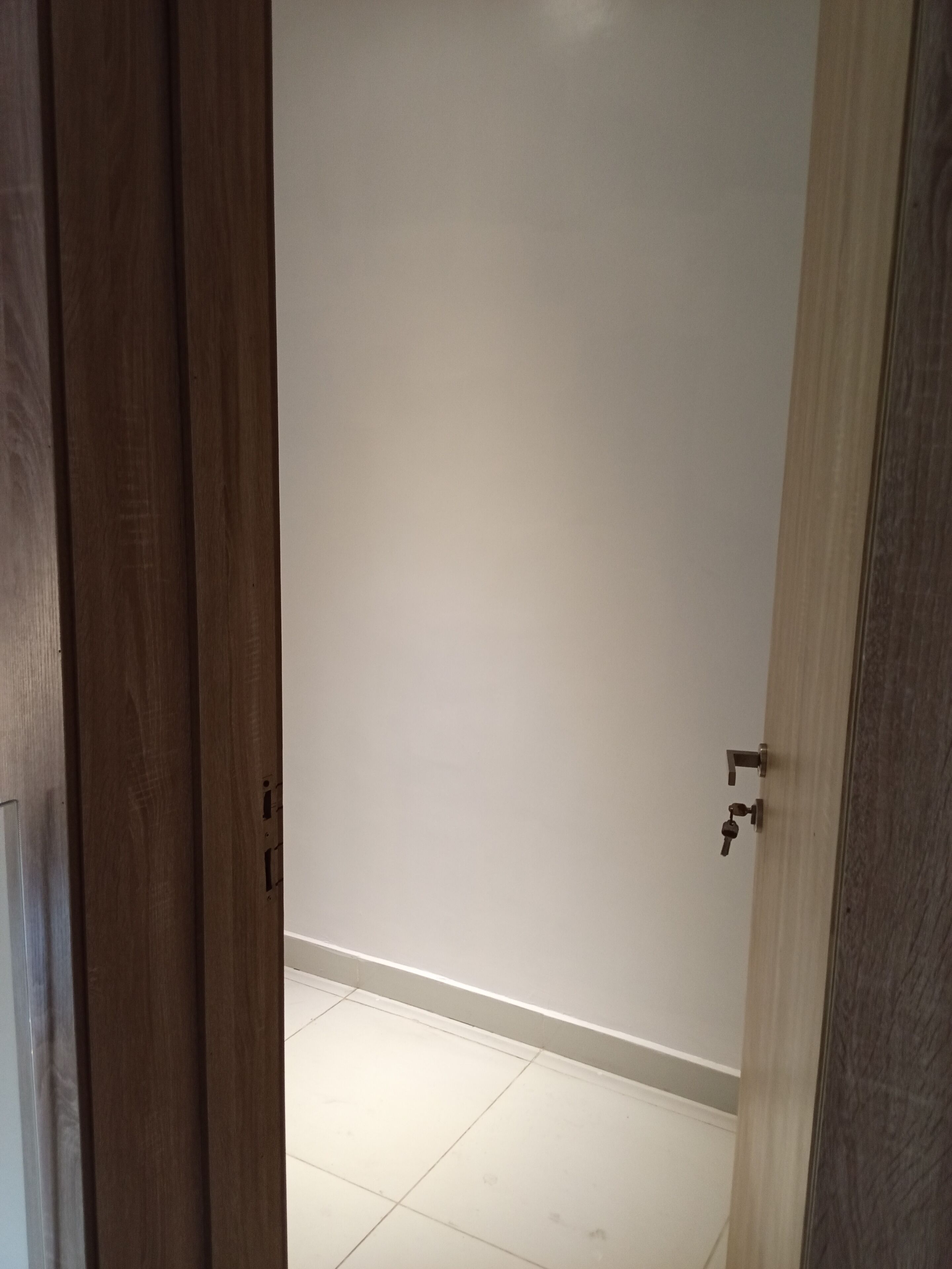 Een kamer met een houten deur, witte muren en een betegelde vloer.