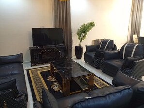 A living room with a sofa, a coffee table, a television, and a potted plant. - Vision Luxury Apartment (Lekki)