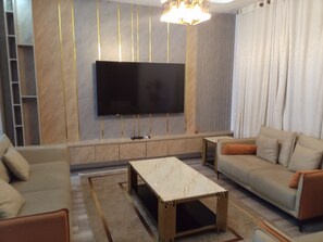 Una sala moderna con una televisión de pantalla plana montada en la pared, un sofá, una mesa de centro y una alfombra estampada.