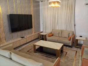 A modern living room with a flat-screen TV, a sofa, a coffee table, and a patterned rug. - Vision Luxury Apartment (Lekki)