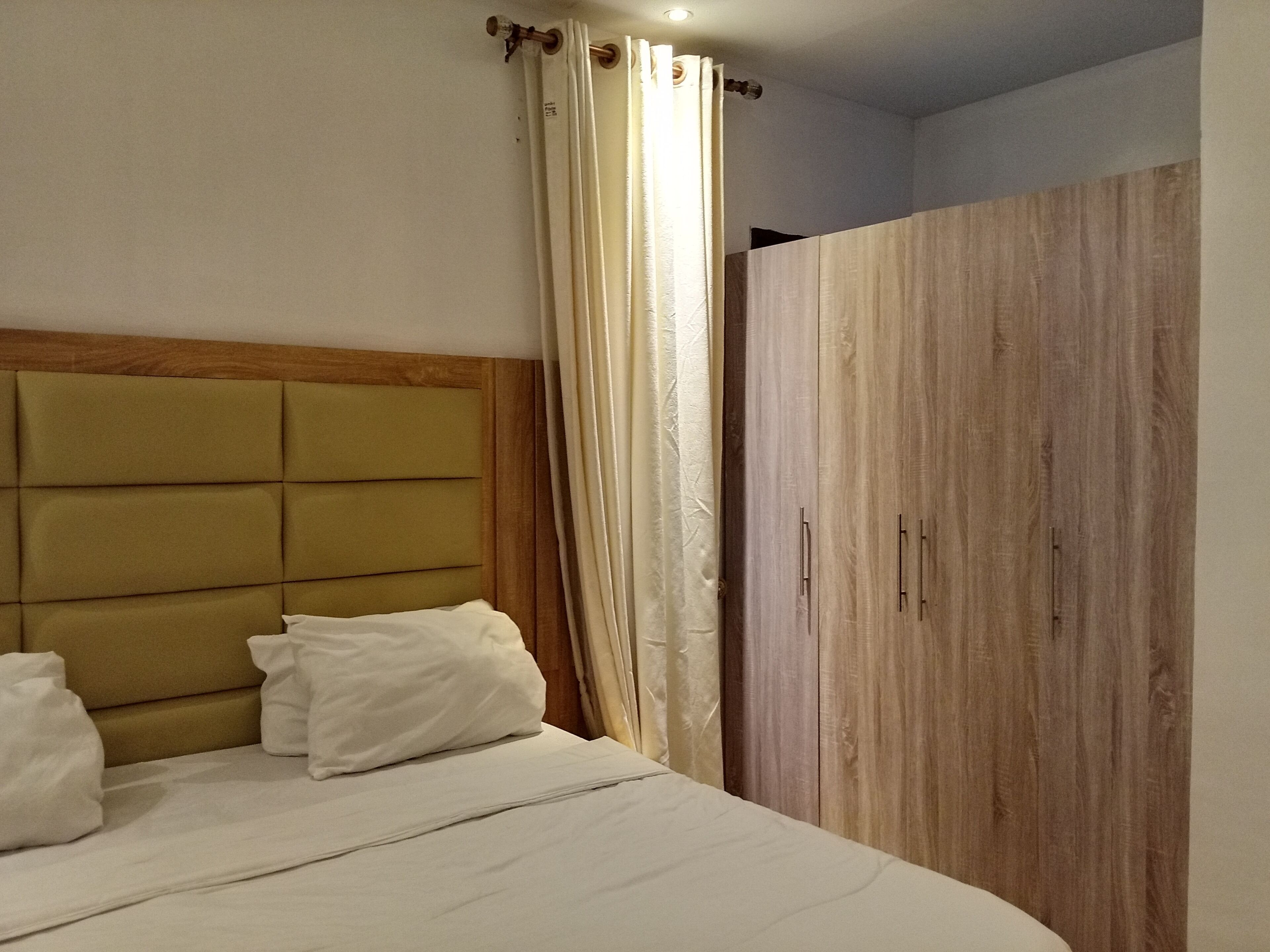 Une chambre à coucher avec un lit, une tête de lit, une armoire et un rideau.