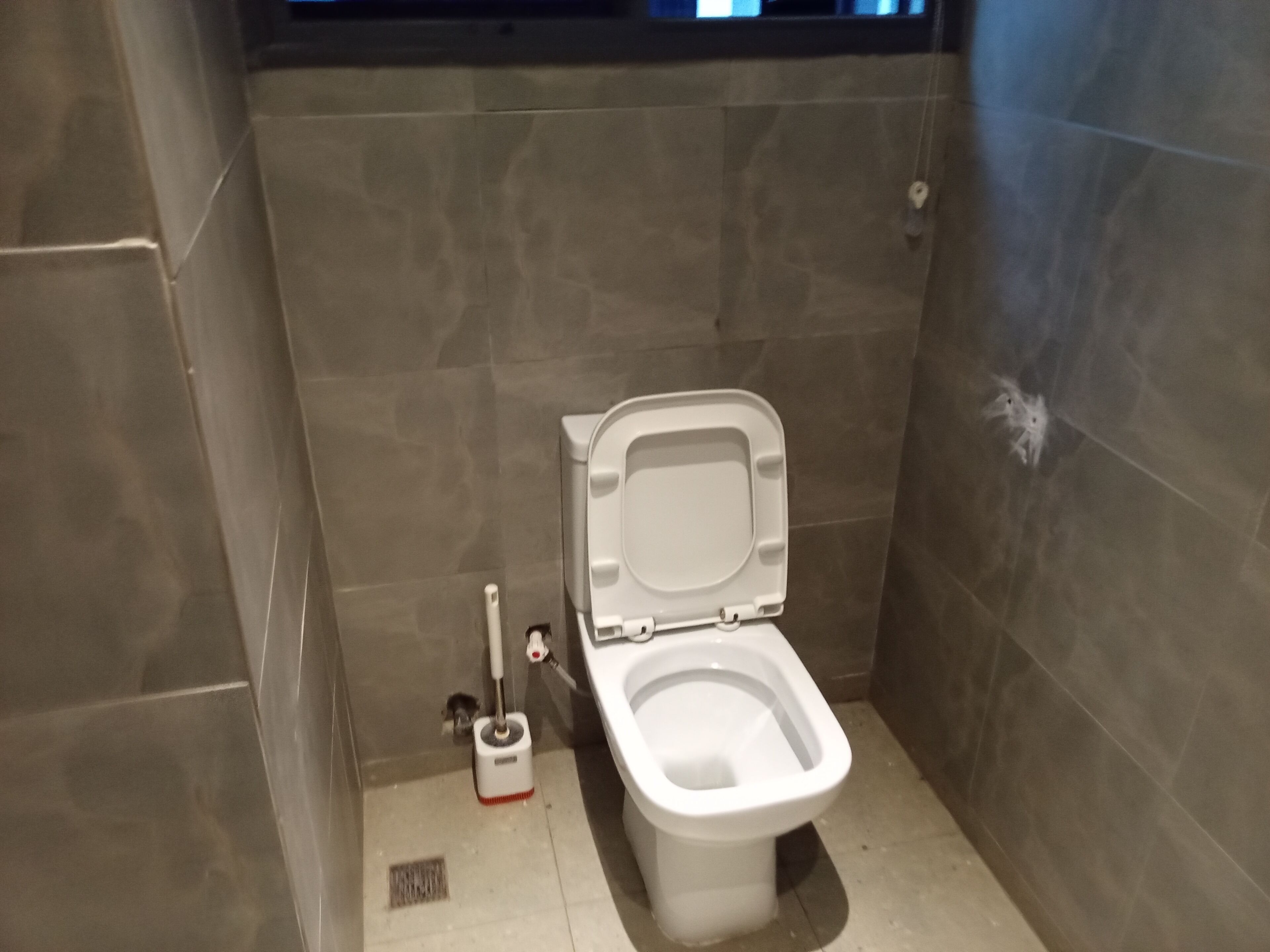 Et lille, moderne badeværelse med toilet, håndholdt bidetbruser og gulvafløb.