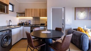A compact kitchen with modern appliances, a dining area with a round table and chairs, and a living space with a sofa and cushions. - Captain's Akaru Hide Away (Sandton)