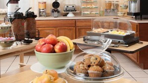 A breakfast buffet with various food items, a coffee station, and a fruit bowl. - City Center Inn (Newport News)