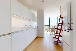 A modern kitchen with white cabinetry, a wooden floor, and a dining area with a table and chairs. - Bright 1BR Home with Shared Terrace-1min to Tube (London)