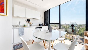 A modern kitchen with white cabinets, a glass dining table, and a view of the city through large windows. - Bright 1BR Home with Shared Terrace-1min to Tube (London)