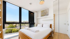 A bedroom with a large window, a bed, a wardrobe, and a painting on the wall. - Bright 1BR Home with Shared Terrace-1min to Tube (London)