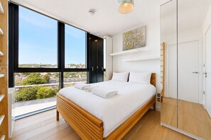 A bedroom with a large window, a bed, a wardrobe, and a painting on the wall. - Bright 1BR Home with Shared Terrace-1min to Tube (London)
