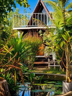 A tropical resort with a wooden deck, lush greenery, and a pond.