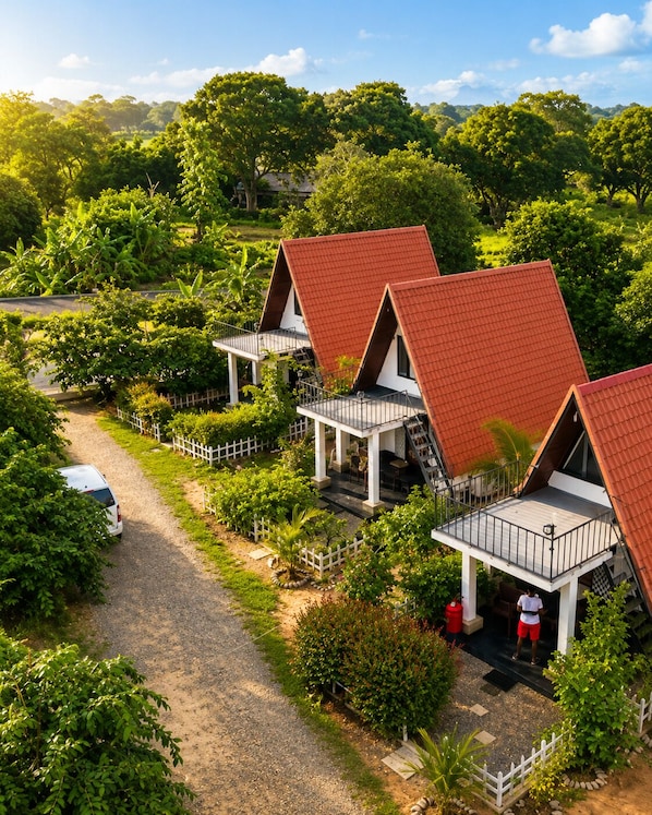 A bungalow-style hotel with a red-tiled roof, a gravel driveway, and a white picket fence surrounding the property.