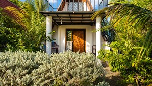 A two-story house with a balcony, surrounded by lush greenery.