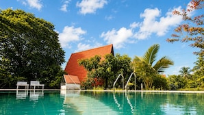 A clear swimming pool with a red-roofed building in the background, surrounded by lush greenery.