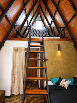 A loft bedroom with a wooden ladder, a bed, a window, and a door.
