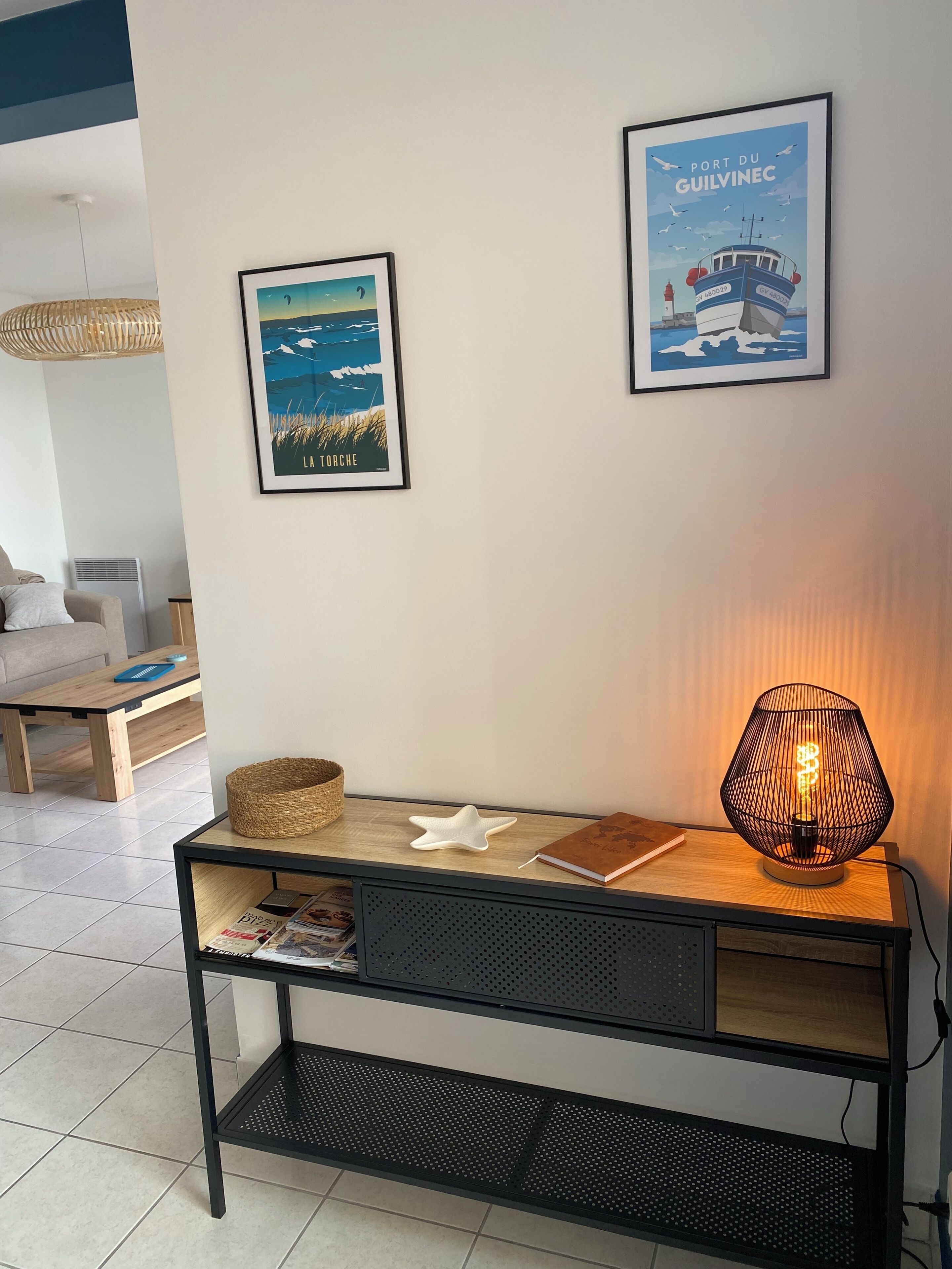 Een moderne woonkamer met een houten console, een geweven mand, een ster-vormig object en een lijst met een kustlandschap.