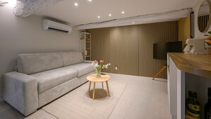 Ein modernes Wohnzimmer mit einer Couch, einem kleinen runden Tisch mit einer Vase, einem Flachbildfernseher und einer Wandpaneele aus Holz.