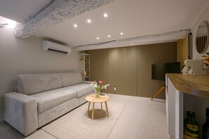 Una sala de estar moderna con un sofá, una mesita redonda con un florero, un televisor de pantalla plana y un panel de pared de madera.