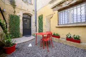 Un patio con una mesa y sillas rojas, una puerta negra y plantas en macetas.