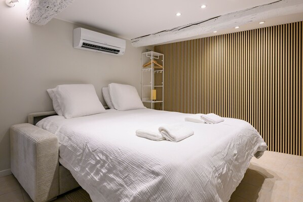 Un dormitorio moderno con una cama grande, ropa de cama blanca, un armario empotrado y un equipo de aire acondicionado.