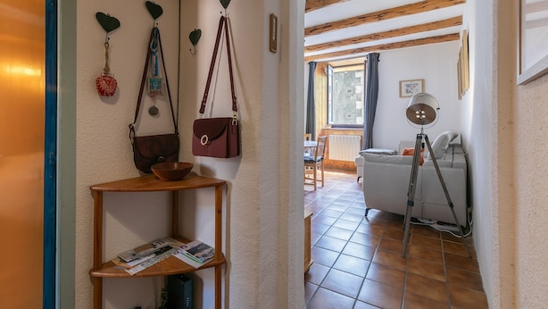 Un pasillo con un estante de madera, una cesta roja y una bolsa marrón colgada de ganchos.