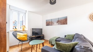 Een woonkamer met een bank, een televisie, een stoel en een raam.
