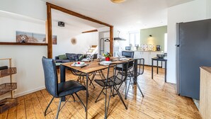 Een moderne keuken met een zwarte koelkast, houten vloer en een eethoek met een houten tafel en zwarte stoelen.