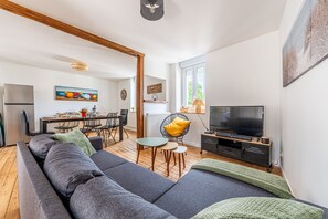 A modern living room with a sofa, TV, dining area, and artwork. - Julice - 1km de la Plage (Langrune-sur-Mer)