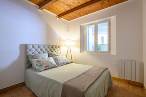 Ein Schlafzimmer mit einer gepolsterten Kopfstütze, floralen Kissen, einer Nachttischlampe, einem Fenster mit Blick und einer Heizung.