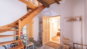 Una scala in legno conduce a una camera da letto soppalcata con soffitto in legno, una sedia, una porta in legno e un appendiabiti.