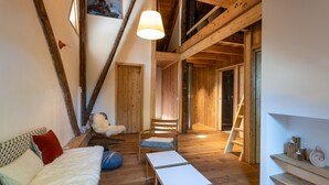 Una stanza in stile loft con travi in legno, un divano bianco, una poltrona e una scala che conduce a un soppalco.