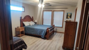 Quarto com cama, mesa de cabeceira, cômoda e ventilador de teto.
