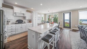 A modern kitchen with white cabinetry, a large island, and a view of the outdoors. - Enjoy stunning Pickwick Lake views and water access from Aqua Vista Pickwick! (Hardin County)