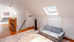 Una habitació amb sostre inclinat, un sofà, una catifes amb dibuixos i un ventilador de sostre.