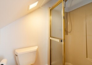 Ein Badezimmer mit Toilette, Dusche mit Glastür und Deckenleuchte.