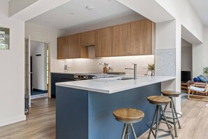 Eine moderne Küche mit Holzausstattung, einer zentralen Kochinsel mit Barhocker und einem Essbereich mit einer Couch und Stühlen.