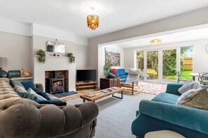 Ein Wohnzimmer mit Kamin, einer Couch, einem Fernseher und Blick auf den Garten durch große Schiebetüren.