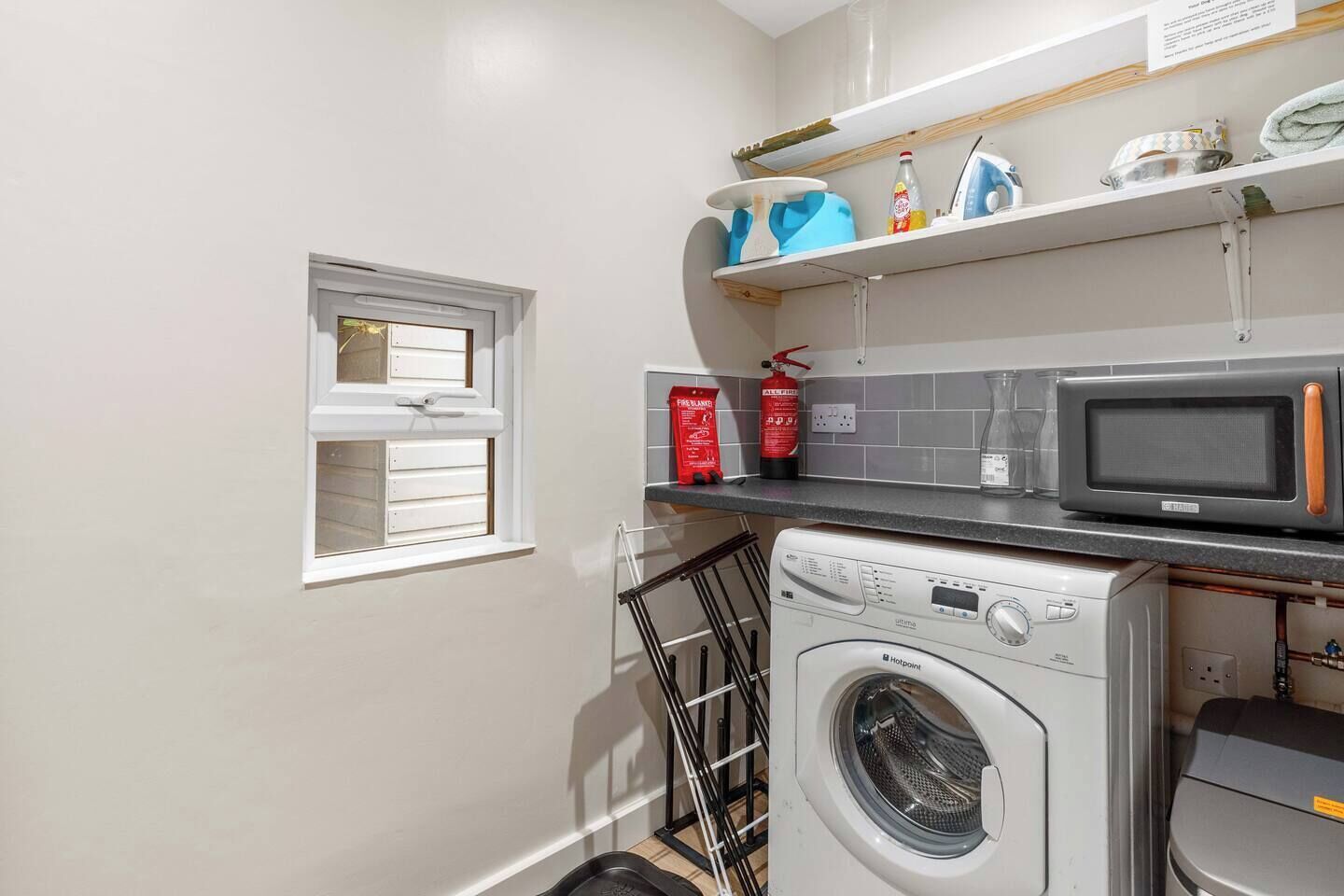 Un espace buanderie équipé d’un lave-linge, d’un four à micro-ondes et d’une fenêtre avec des stores.