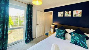 A bedroom with a bed, a nightstand, a lamp, and a view of the outside. - Sociable Suffolk Home | A12, Ipswich & Colchester (Capel Saint Mary)