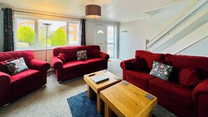 A living room with two red sofas, a wooden coffee table, and a large window with a view of greenery. - Sociable Suffolk Home | A12, Ipswich & Colchester (Capel Saint Mary)
