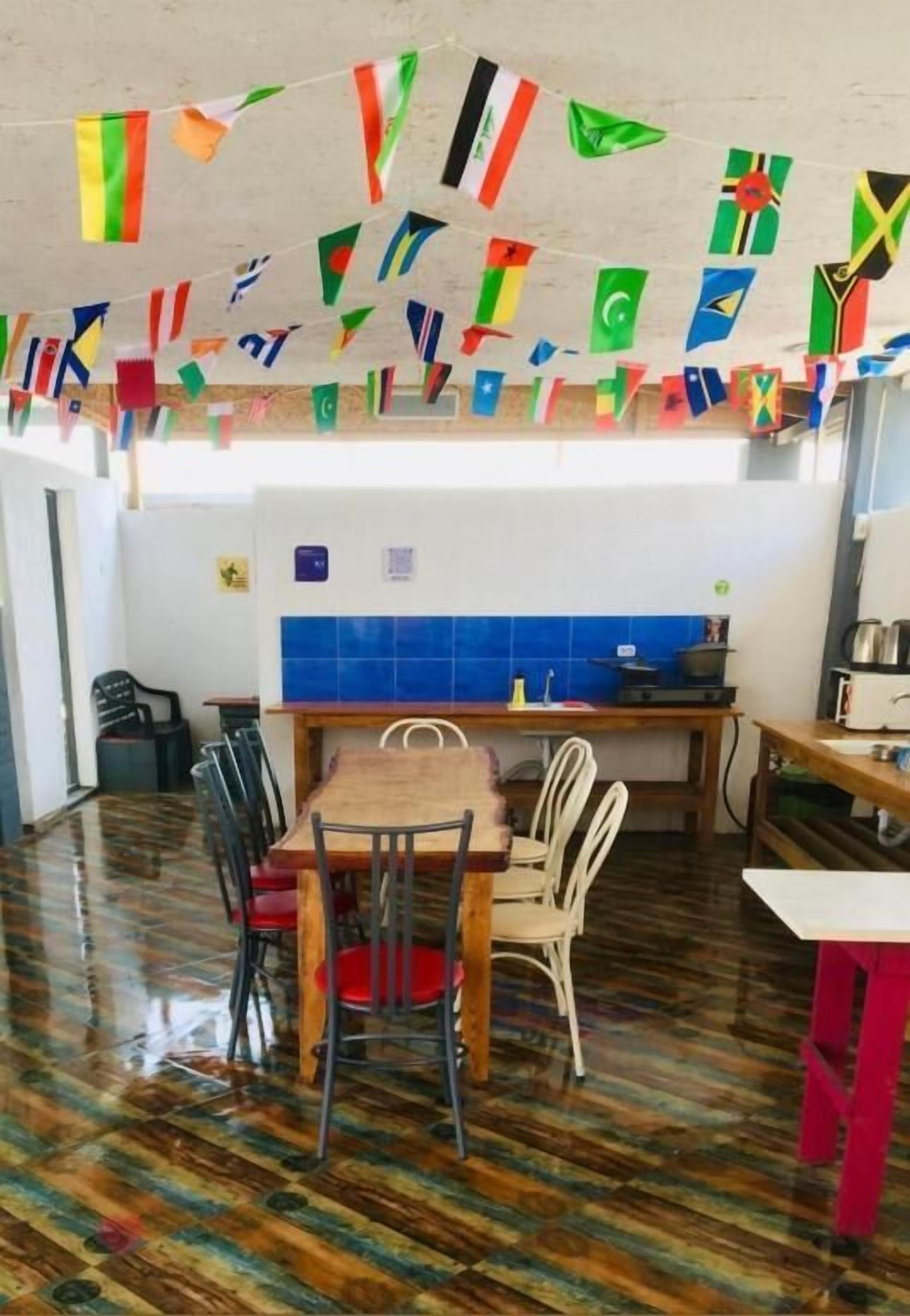 A dining area with a wooden table and chairs, a tiled backsplash, and a variety of flags hanging from the ceiling.