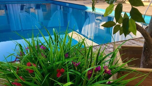 Una piscina con bordo in legno, tende bianche e sedie a sdraio.