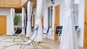 Area relax esterna coperta con lettini e ombrelloni, pavimento in legno e un design architettonico semplice ed essenziale.