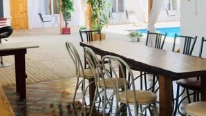 Zona pranzo con tavolo e sedie in legno, una pianta in vaso e vista sulla piscina. Sono appese bandiere al soffitto.